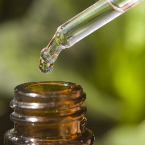 Macro shot of a pipette over a bottle, with a plant creating a soft coloured background.